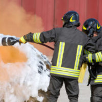 Two Firefighters In Action With Foam firefighters in action with foam to put out the fire of the car